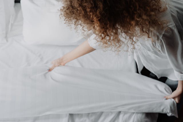 Cleaner making a guest bed with fresh white linens